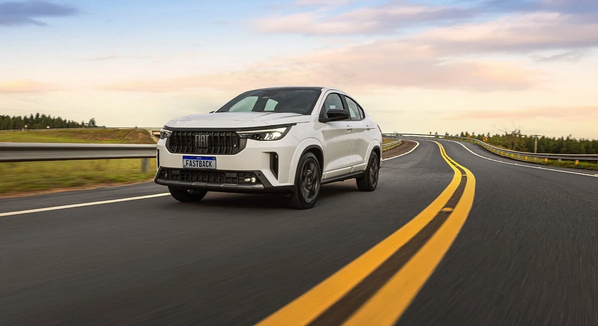 Fiat Fastback branco da linha 2026 em movimento numa rodovia, visto de frente em três quartos, com a grade e a placa de identificação Fastback
